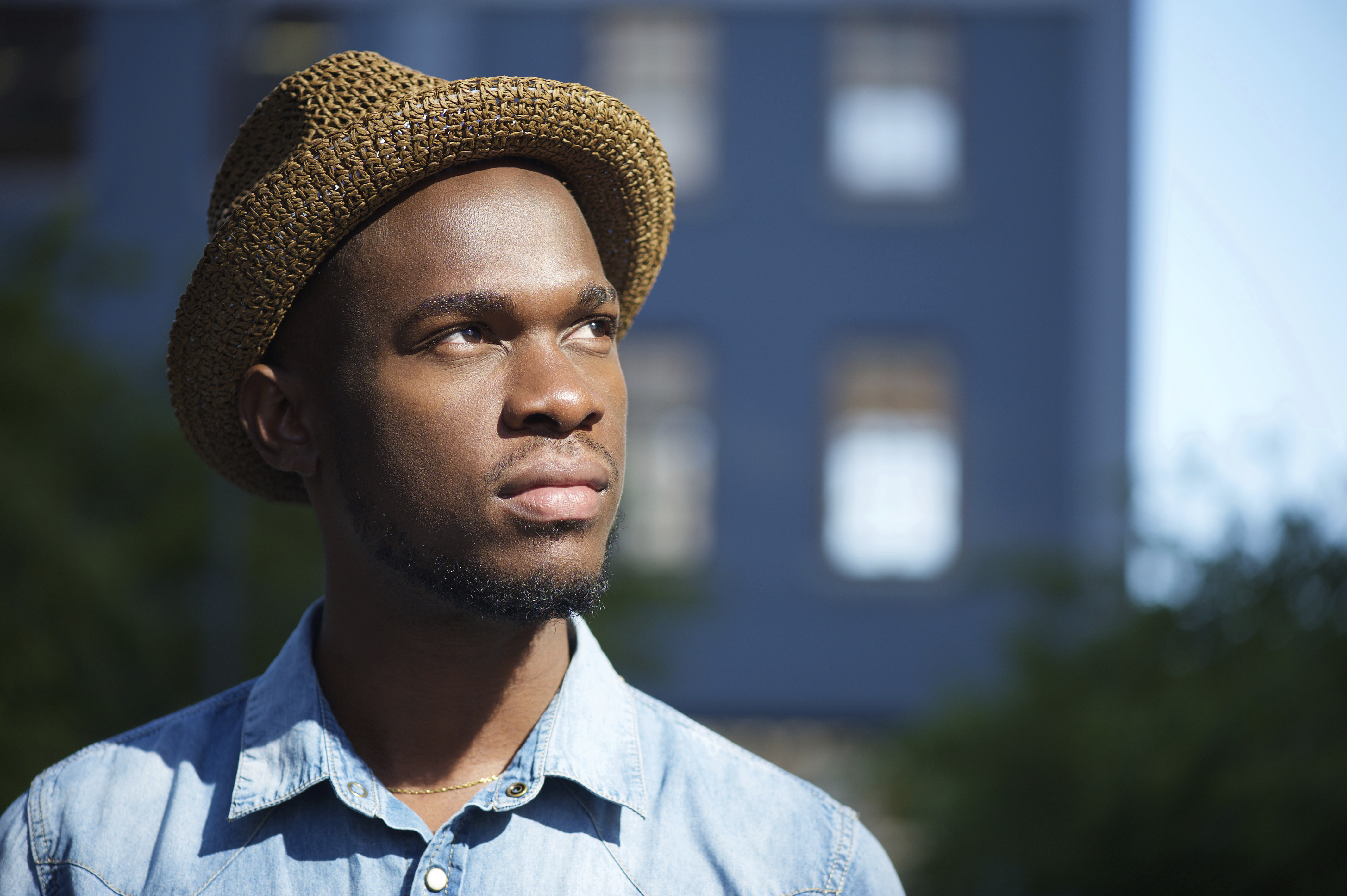 Close up of a young man wearing a hat, building in background.