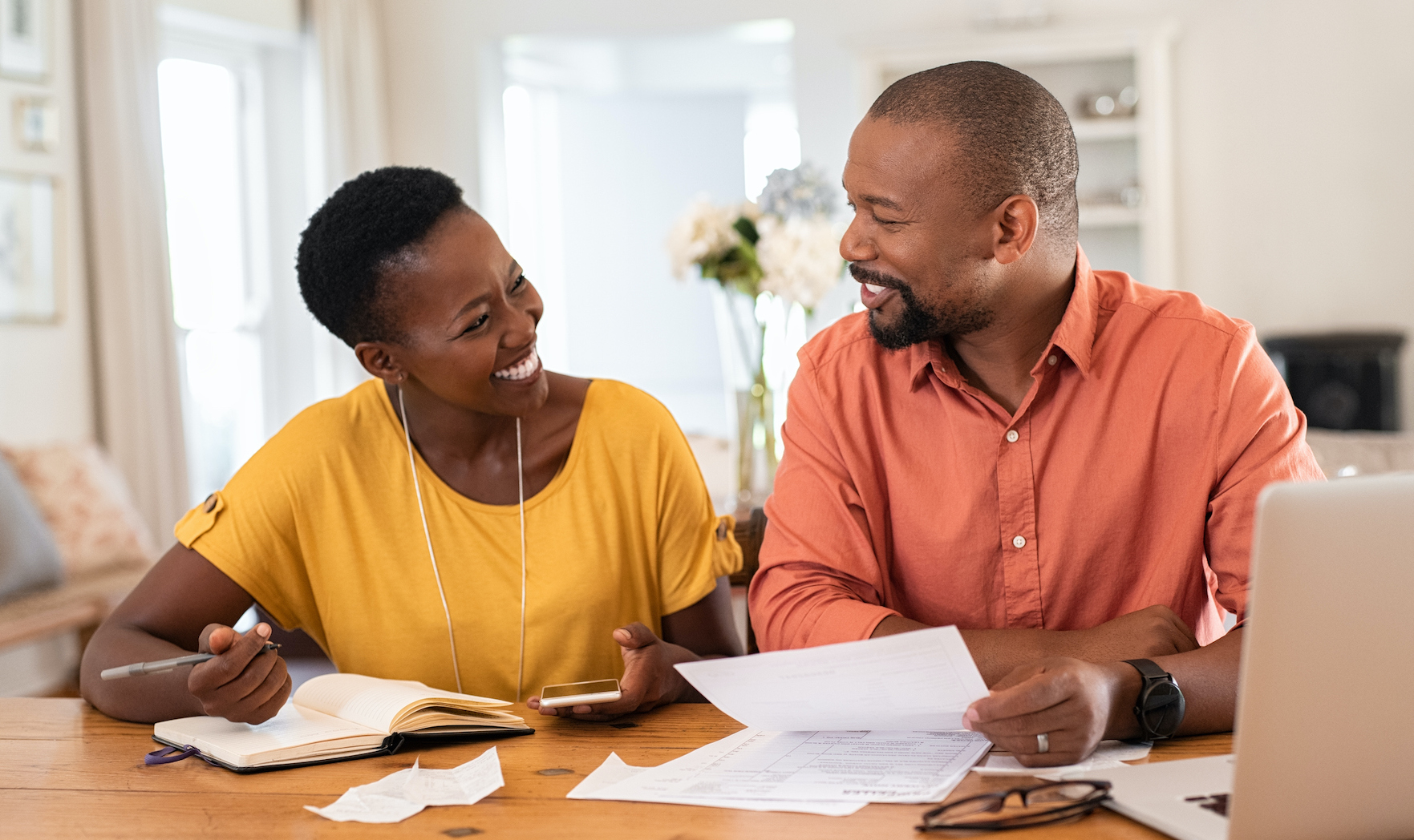 Cheerful mature couple sitting and managing expenses at home. Happy african man and woman paying bills together and managing budget. Black smiling couple checking accountancy and bills while looking at each other. (Cheerful mature couple sitting and m