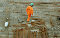 A construction worker in a green helmet and orange jumpsuit on the worksite.