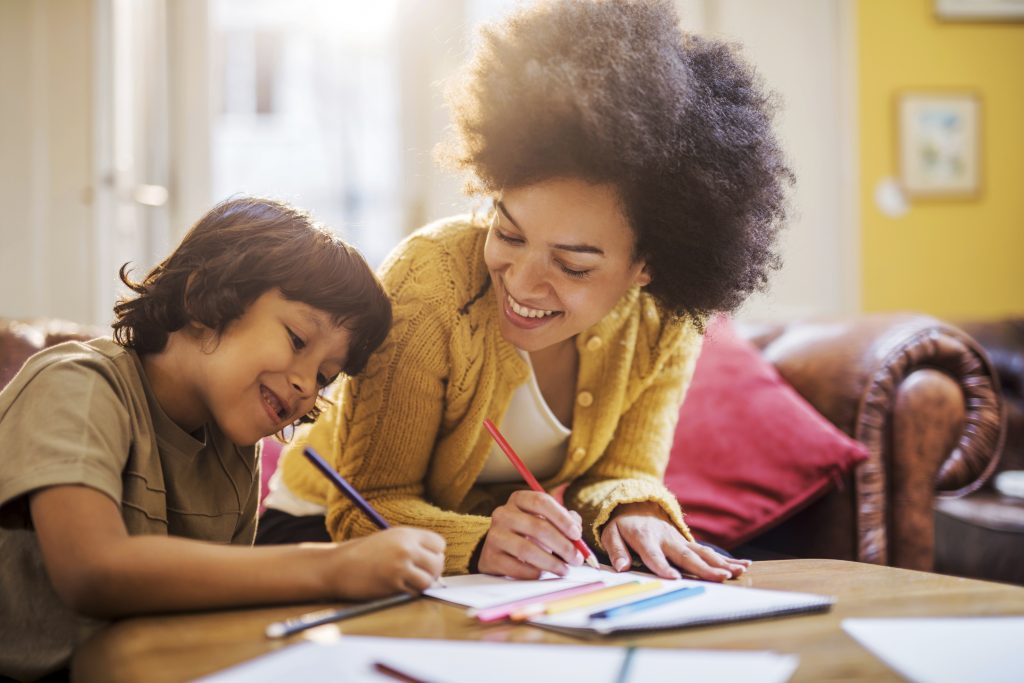 Young happy African American mother having fun with his son at home while coloring together.