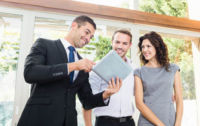 A real estate agent shows two clients listing information on a tablet.